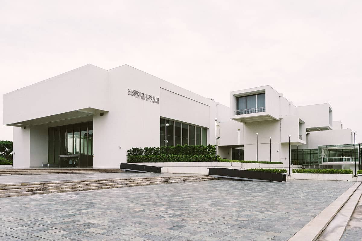 Weitwinkelaufnahme der Außenfassade des Taipei Fine Arts Museum mit seiner modernen weißen Würfelarchitektur und dem Museumsnamen auf Englisch und Chinesisch.
