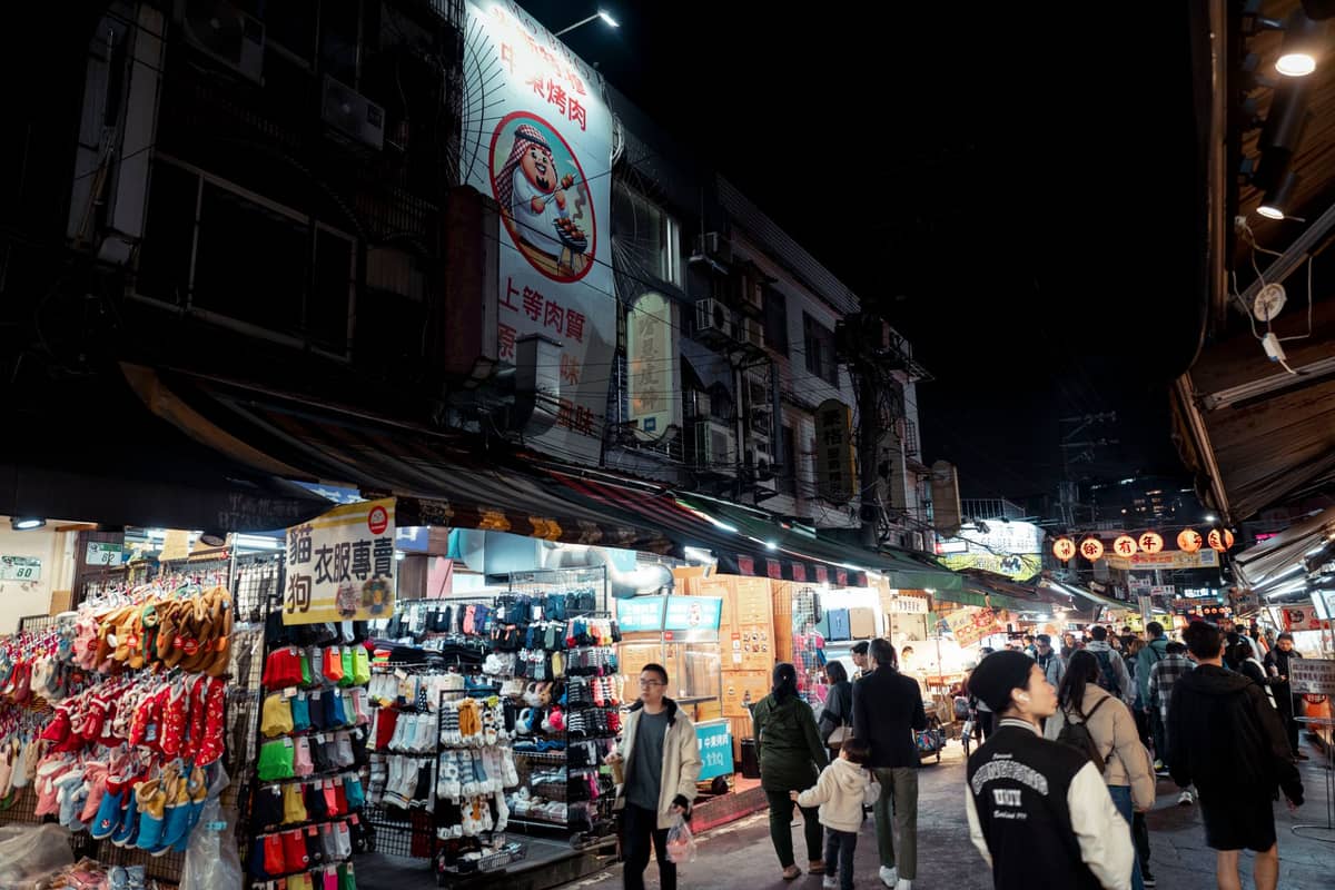 Lebhafte Nachtmarktszene in Taipei mit Menschenmassen, hell erleuchteten Ständen und leuchtenden Schildern unter dem Nachthimmel.