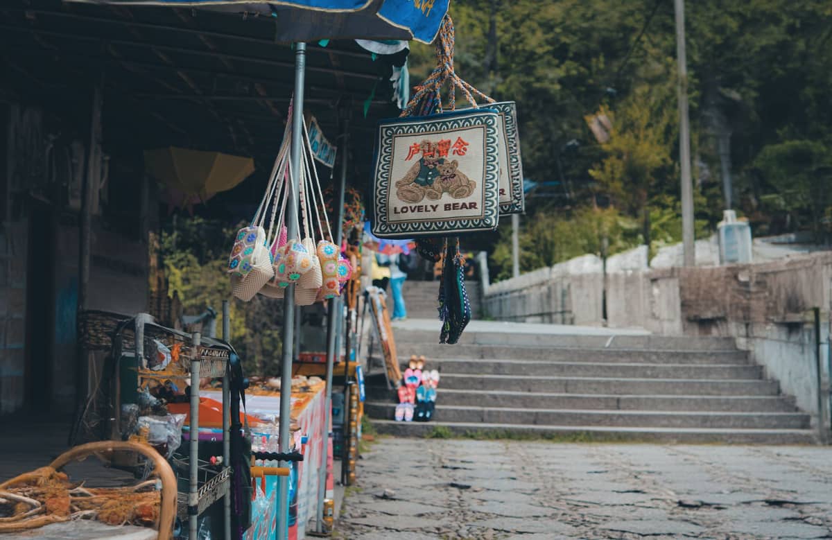 Marktstand in Wulai mit hängenden indigenen Kunsthandwerken und Souvenirs, Steinstufen und Grünpflanzen im Hintergrund.