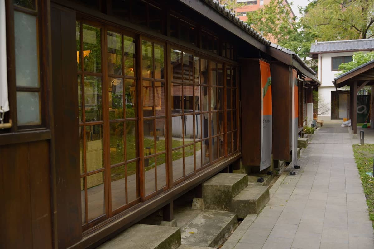 Reihe traditioneller hölzerner Gebäude aus der japanischen Ära und Fußweg in Beitou, Taipei, umgeben von Grünflächen und offenen Fenstern.