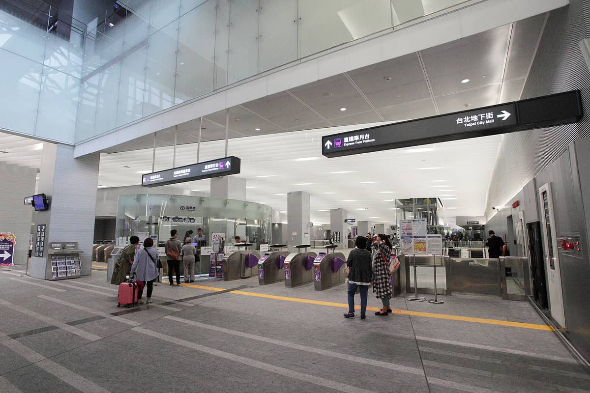 Reisende mit Gepäck am Eingang und den Fahrgasttoren der Taoyuan Airport MRT-Station, mit klaren Hinweisschildern zu den Expressbahnsteigen.