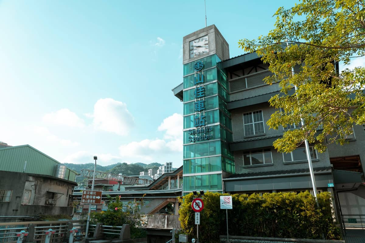 Modernes Glasgebäude mit Uhrturm, chinesischen Schildern, Grünpflanzen und blauem Himmel im Jinguashi Gold Museum.