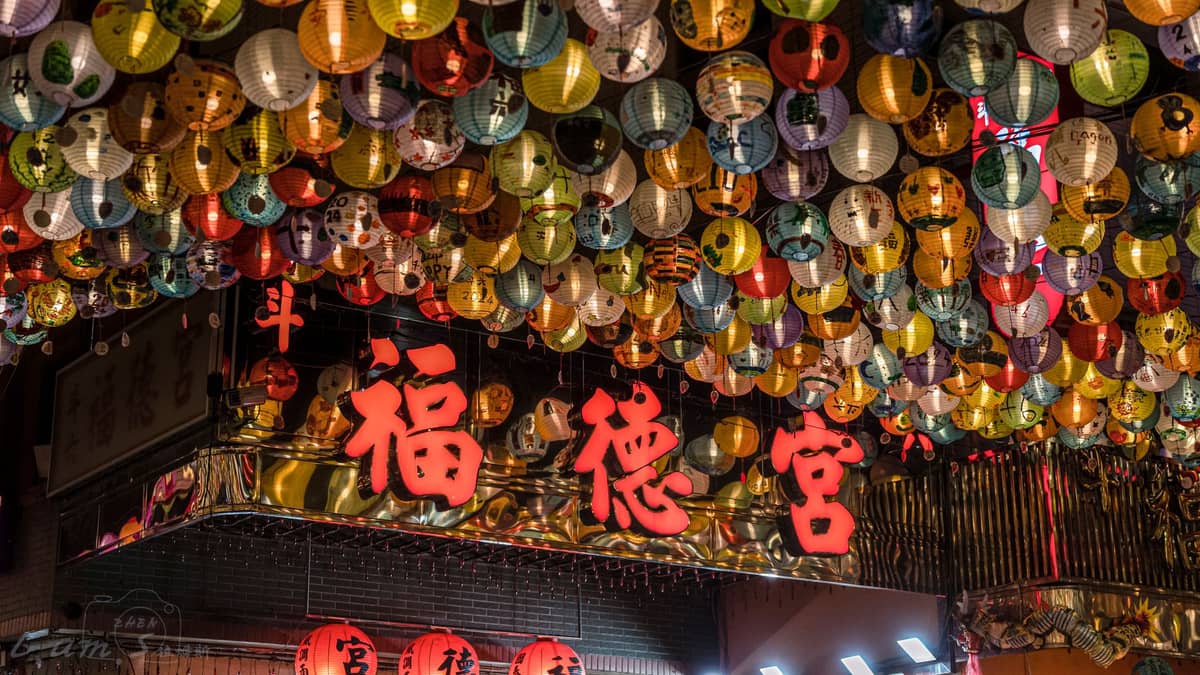 Nächtliche Szene mit vielen bunten Laternen, die über einer Straße mit rot beleuchteten chinesischen Schriftzeichen hängen, festliche Atmosphäre im städtischen Taiwan.