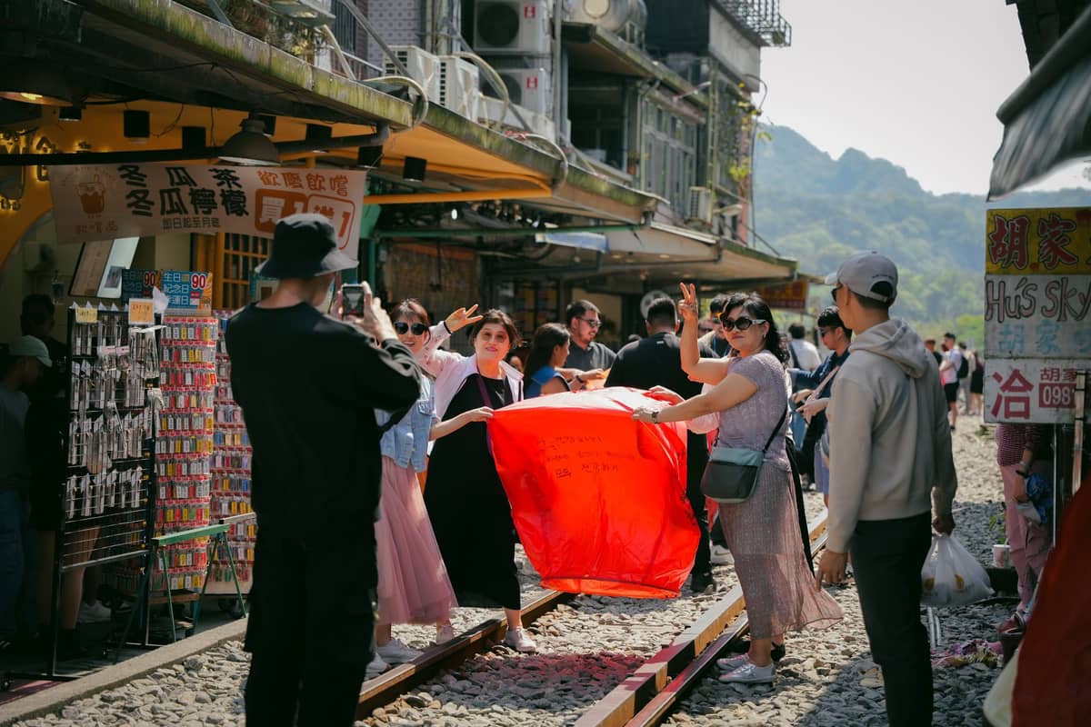 Touristen halten eine Himmelslaterne auf den Bahngleisen in Shifen in Pingxi – ein typisches Bild beim Pingxi Sky Lantern Festival und den täglichen Laternenaufstiegen.