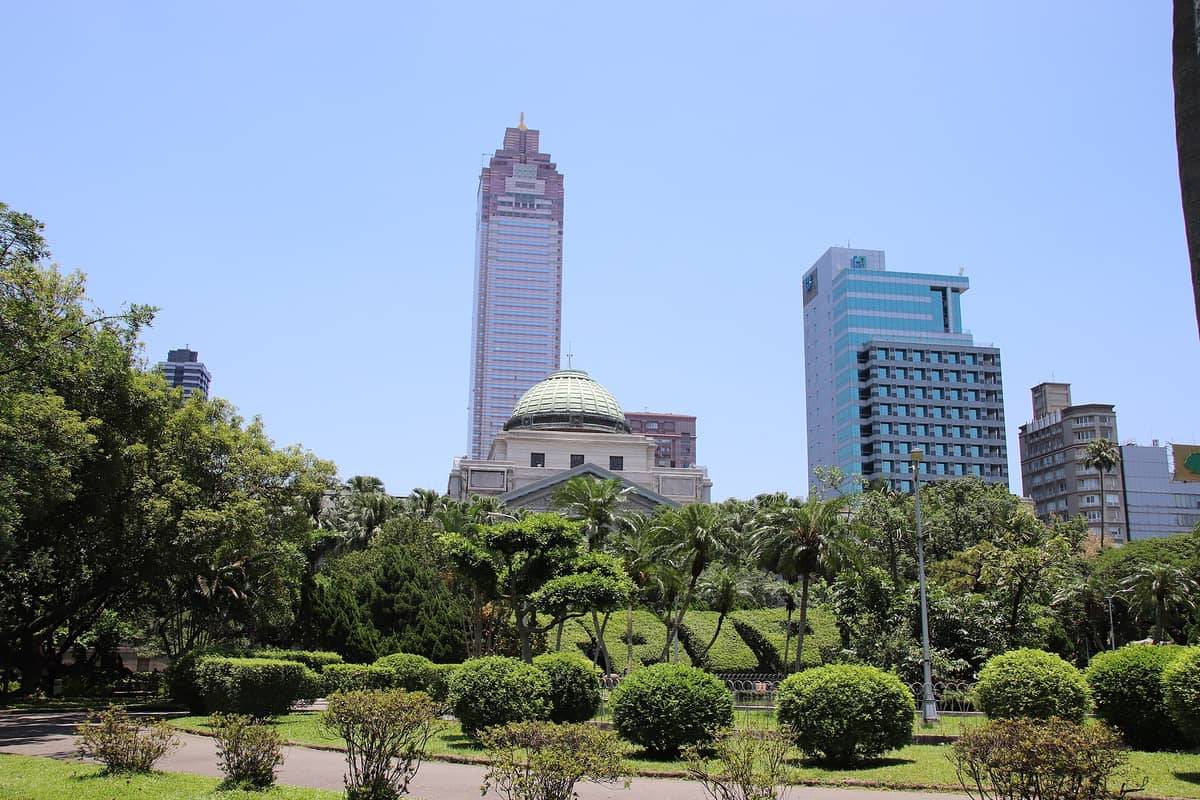 Außenansicht des National Taiwan Museum mit grüner Kuppel, umgeben von Bäumen und modernen Wolkenkratzern Taipeis im Hintergrund.