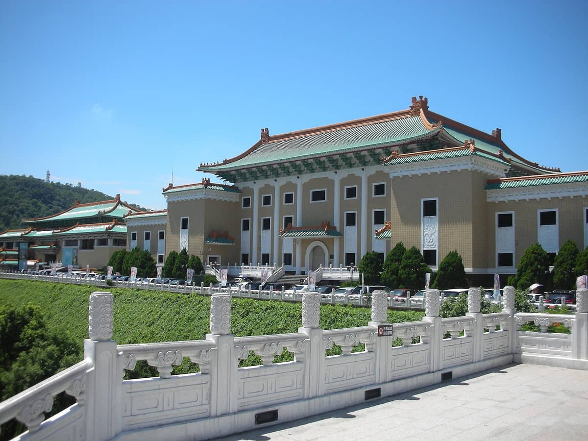 Panoramablick auf das Nationale Palastmuseum in Taipeh mit klassischer chinesischer Architektur, grün gekachelten Dächern und einem Hügel im Hintergrund unter strahlend blauem Himmel.