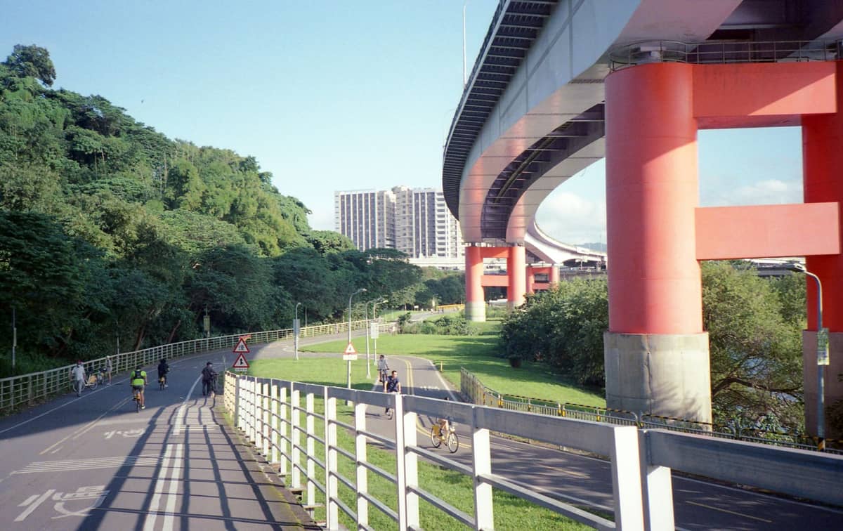 Menschen auf einem Fahrradweg am Flussufer unter einer Schnellstraße in Taipei an einem sonnigen Tag
