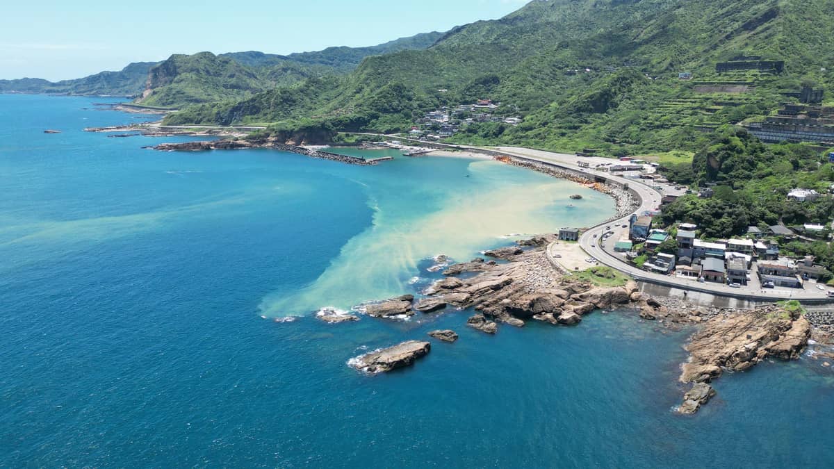 Luftaufnahme des Yehliu Geoparks: Die dramatische Landzunge der Nordküste ragt ins blaue Meer, im Hintergrund geschwungene Zufahrtsstraßen und grüne Hügel.