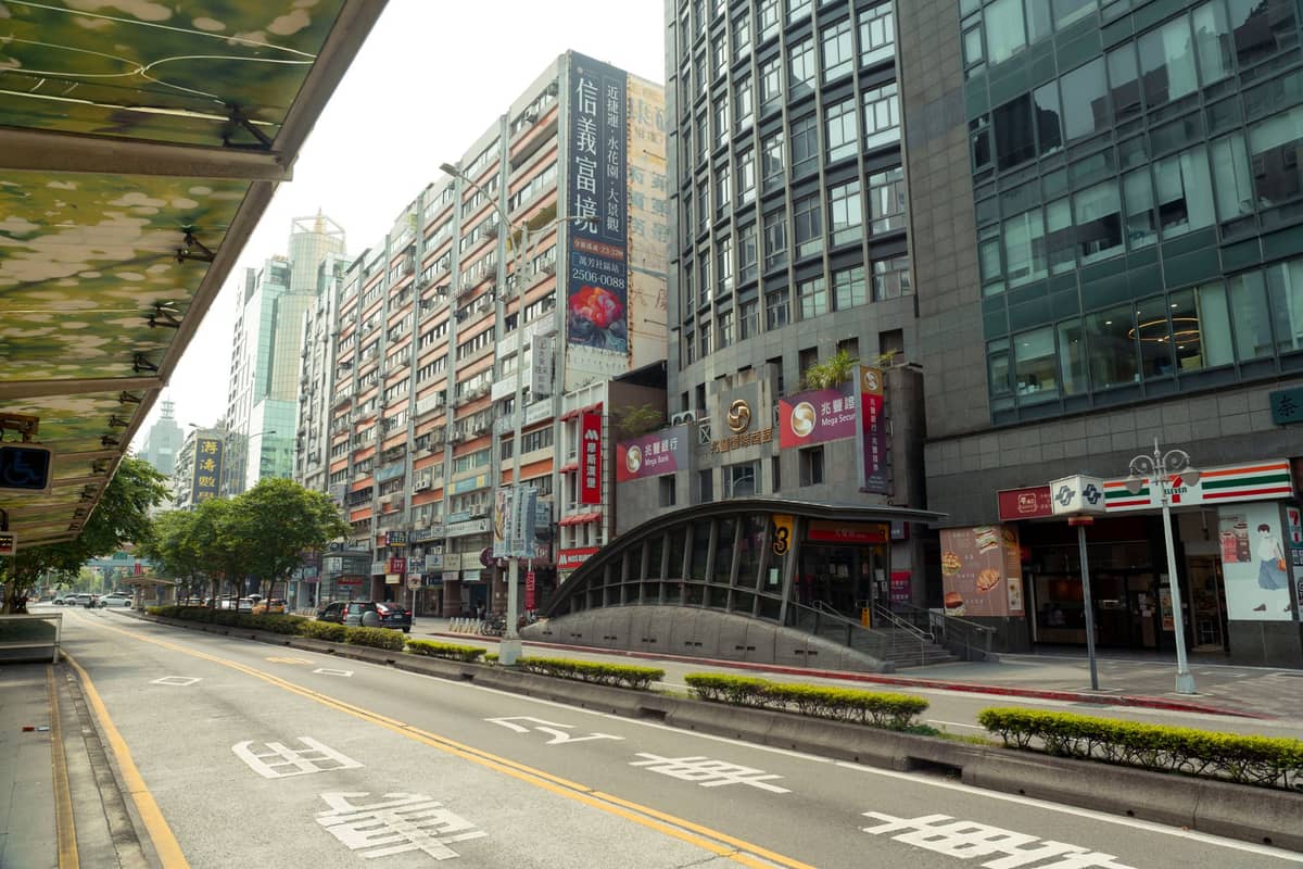 วิวถนนในไทเปพร้อมโรงแรมท้องถิ่นขนาดกลาง ร้านสะดวกซื้อ และทางเข้าสถานี MRT โดยตรง เหมาะสำหรับนักท่องเที่ยวงบประมาณจำกัด
