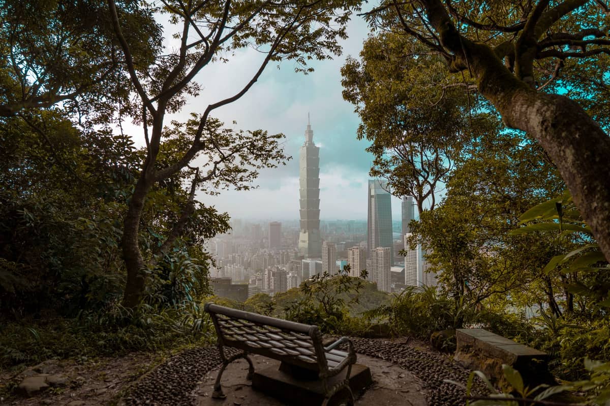 Bank mit Blick auf die Skyline von Taipei mit dem Taipei 101, eingerahmt von Bäumen und Grünflächen, die einen ruhigen und gemächlichen Morgen heraufbeschwören.