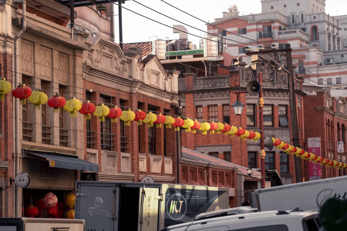 Historische rote Backsteingeschäftshäuser mit hängenden Laternen in einer belebten Straße im alten Kaufmannsviertel von Taipei, mit einer Mischung aus alten und modernen Gebäuden.