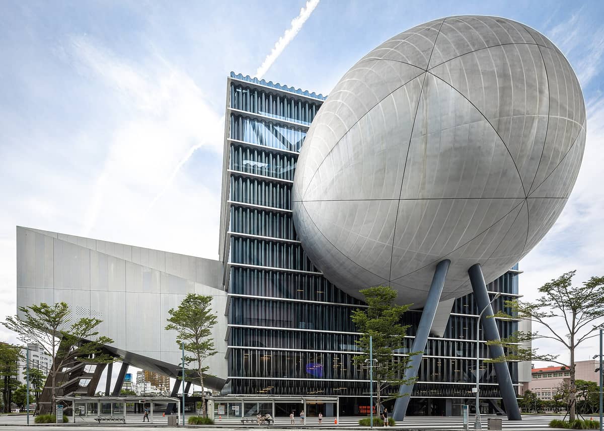 Die markante Architektur des Taipei Performing Arts Center mit seiner auffälligen silbernen Kugel und der geometrischen Fassade, vom Vorplatz bei Tageslicht aufgenommen.