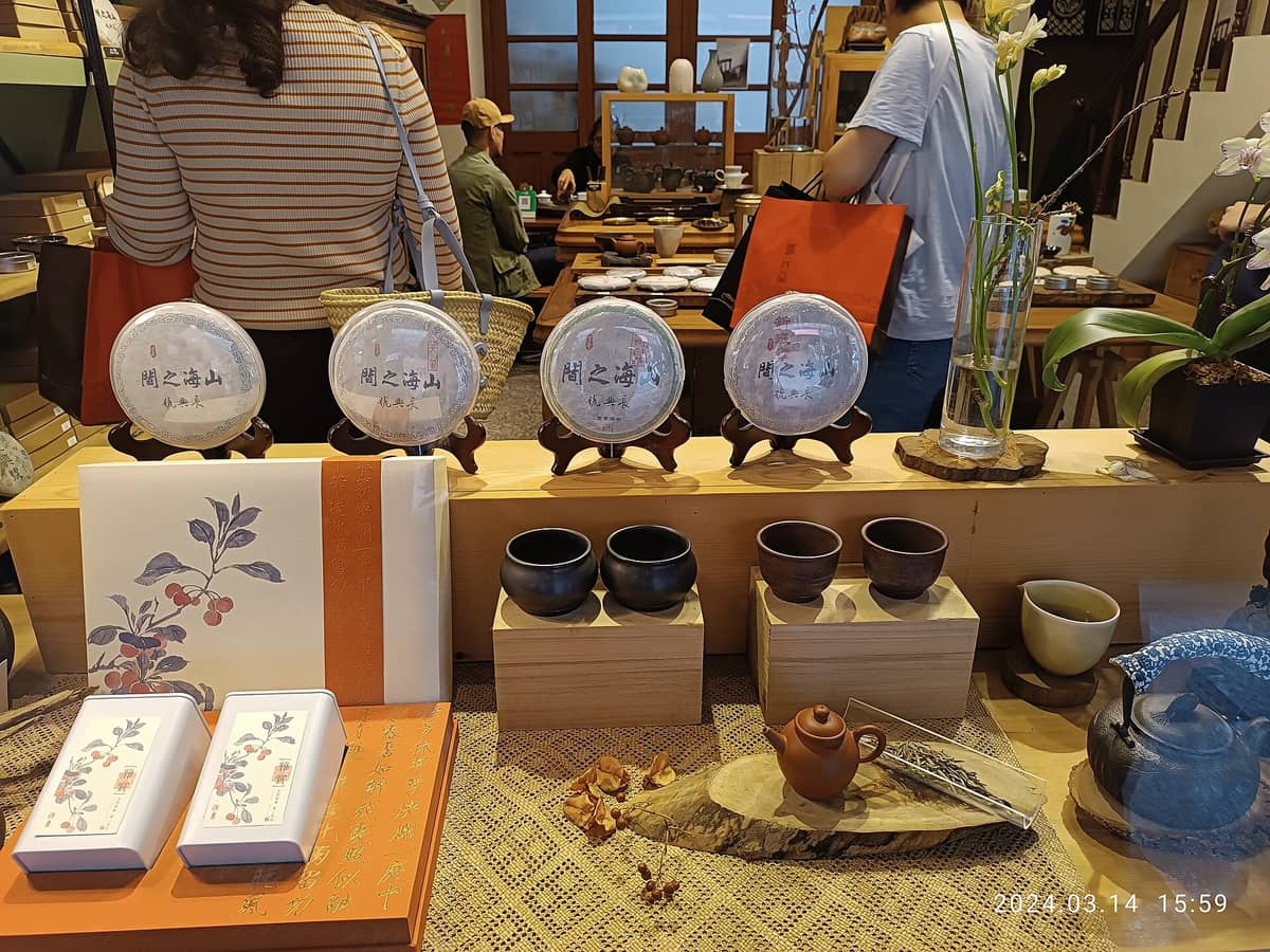 Ausstellung von Spezialteekuchen und Teeutensilien in einem Geschäft in Taipei mit Kunden, die im Hintergrund Regale mit Keramik und Teegeschenken durchstöbern.