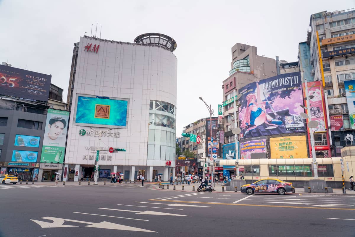 Weitläufiger Blick auf Ximending in Taipei mit bunten Werbetafeln, bekannten Geschäften wie H&M und einem belebten Fußgängerbereich.