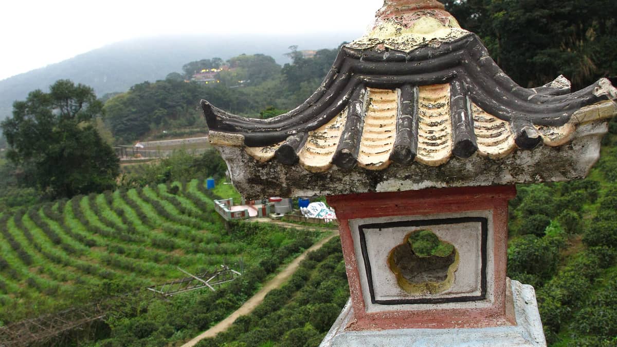Nahaufnahme eines traditionellen chinesischen Architekturelements mit Blick auf Teeplantagen an einem üppig grünen Hang in Maokong, Taipei, an einem nebligen Tag.