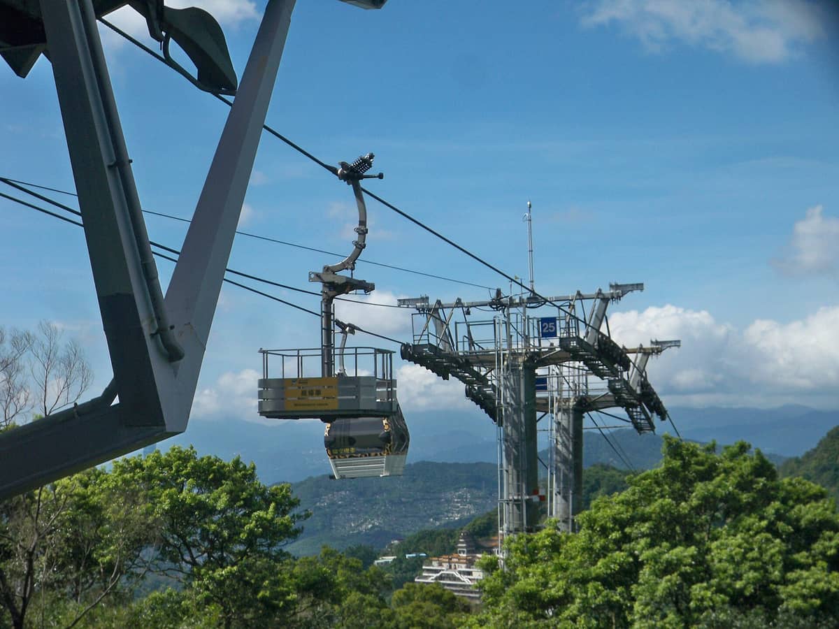 Eine Gondel mit Glasboden der Maokong Gondola gleitet über grüne Hügel mit blauem Himmel und Bergen im Hintergrund.