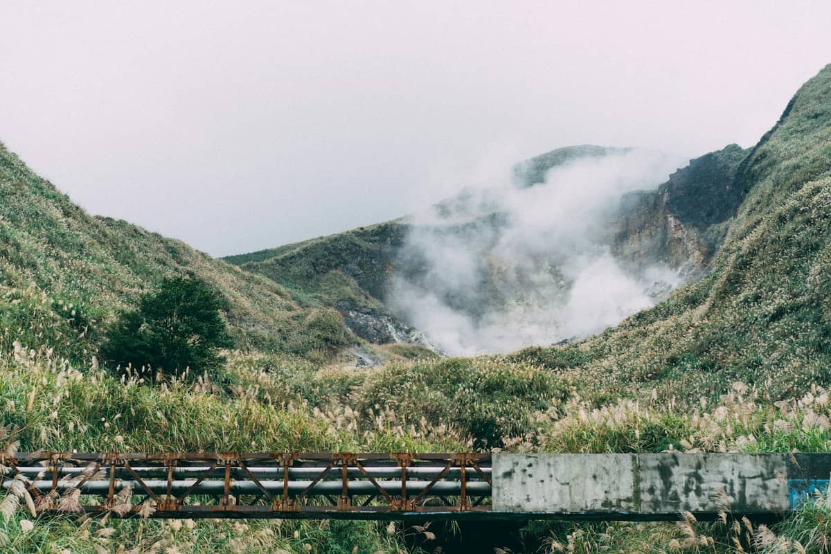 Dampf steigt aus einem Vulkankrater auf, der von üppig grünen Hügeln im Yangmingshan-Nationalpark nahe Taipei umgeben ist.