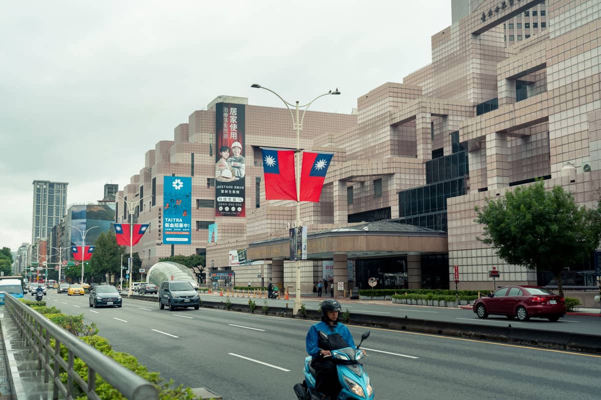 Straßenansicht des National Palace Museum in Taipei mit Taiwan-Flaggen und Menschen auf Rollern und in Autos.