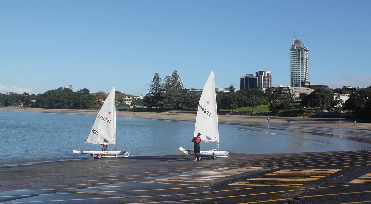 Takapuna Beach mit seinem Sandstrand, ruhigem Wasser, Segelbooten und dem markanten Sentinel-Apartmentgebäude im Hintergrund auf Aucklands North Shore.