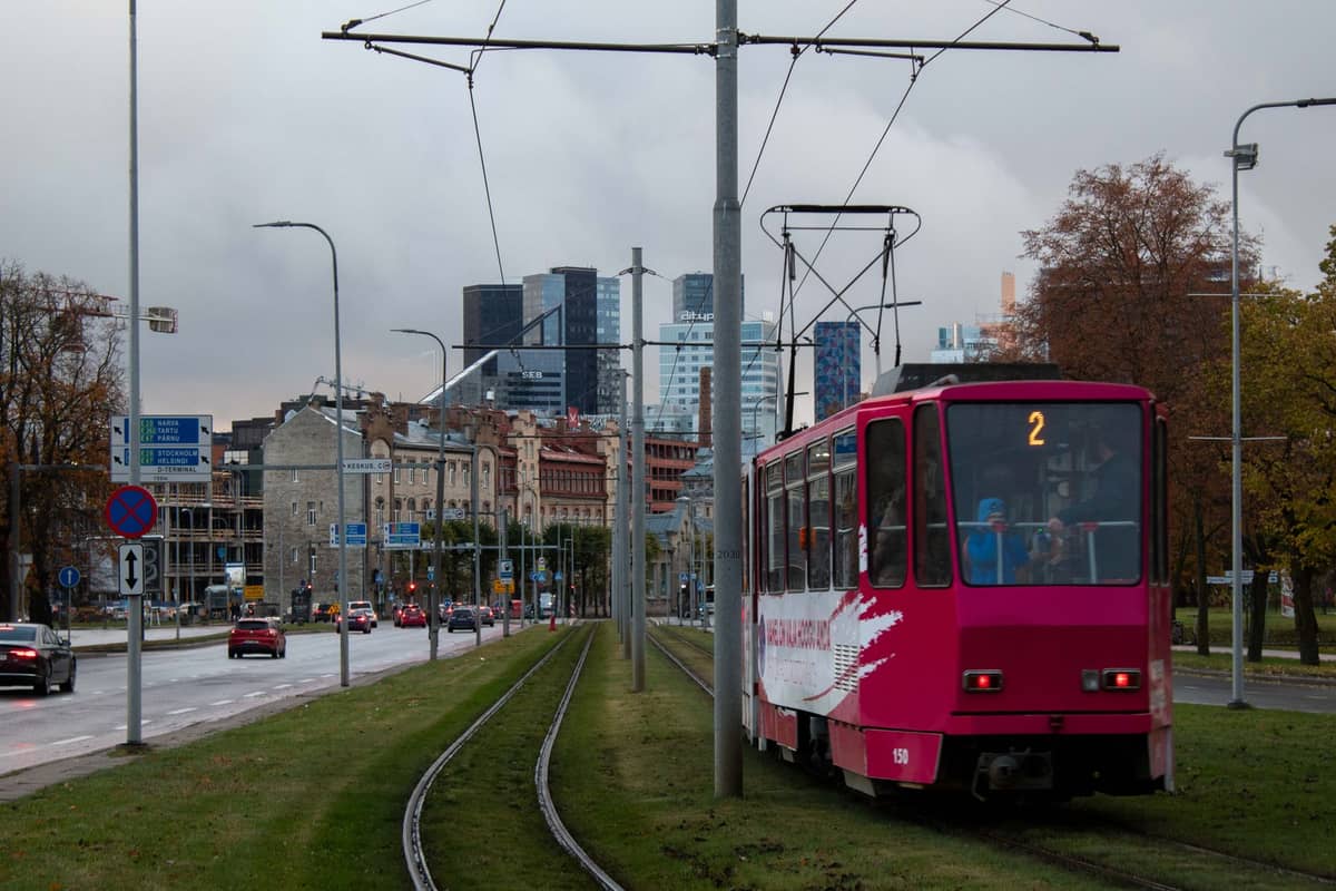 Um eléctrico rosa de Tallinn em trilhos separados por grama com o horizonte da cidade de Tallinn ao fundo sob céus nublados.
