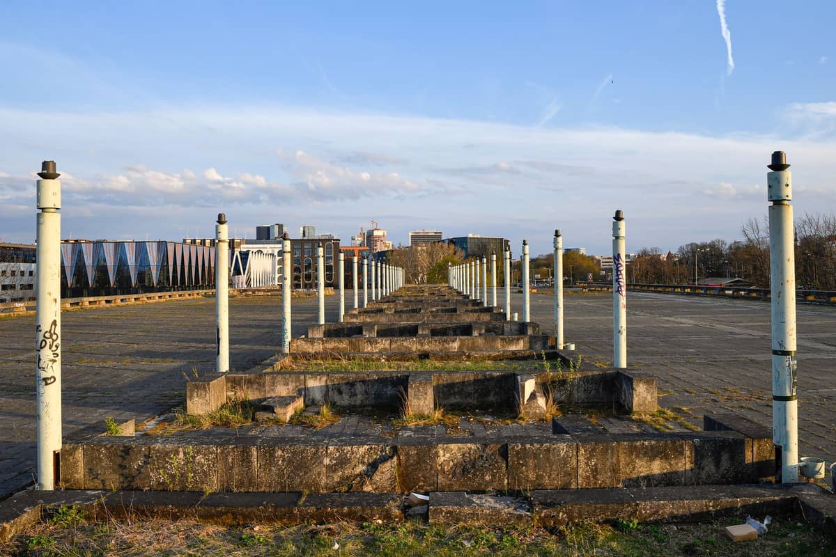 Vista ampia di un grande anfiteatro brutalista in cemento vuoto sul lungomare di Tallinn, con gradini consumati, pali e edifici della città sullo sfondo.