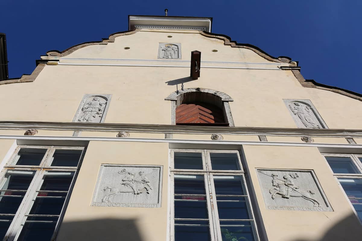 Fassade des Hauses der Schwarzenhäupter in Tallinn mit cremeweißen Wänden, drei skulptierten Steinreliefs, großen Fenstern und blauem Himmel.