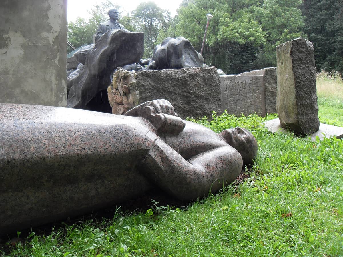 Gestürzte Statue aus der Sowjetzeit auf dem Gras mit weiteren Steindenkmälern und Skulpturen im Hintergrund im Maarjamäe-Memorialkomplex in Tallinn.