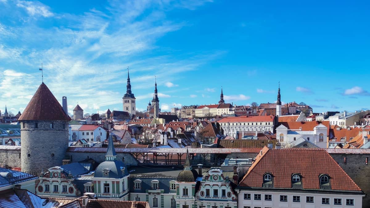 Panoramablick auf die Tallinner Altstadt mit mittelalterlichen Steinmauern, Türmen und roten Ziegeldächern unter einem strahlend blauen Himmel.