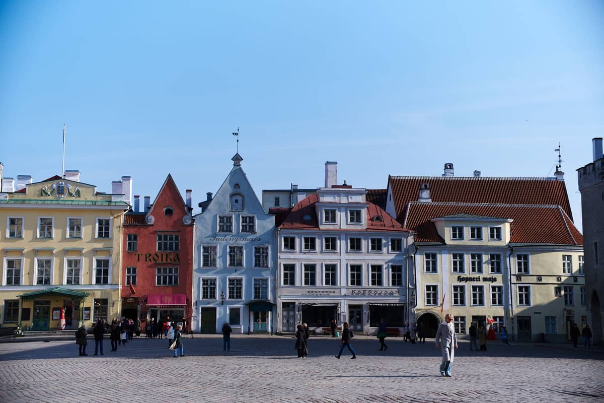 Altstadtplatz von Tallinn mit bunten hanseatischen Kaufmannshäusern und Kopfsteinpflaster unter blauem Himmel, Menschen spazieren und versammeln sich.