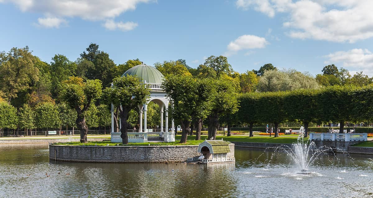 Parco Kadriorg a Tallinn con un padiglione a cupola, giardini formali, uno stagno con una fontana e rigogliosi alberi verdi in una giornata di sole.