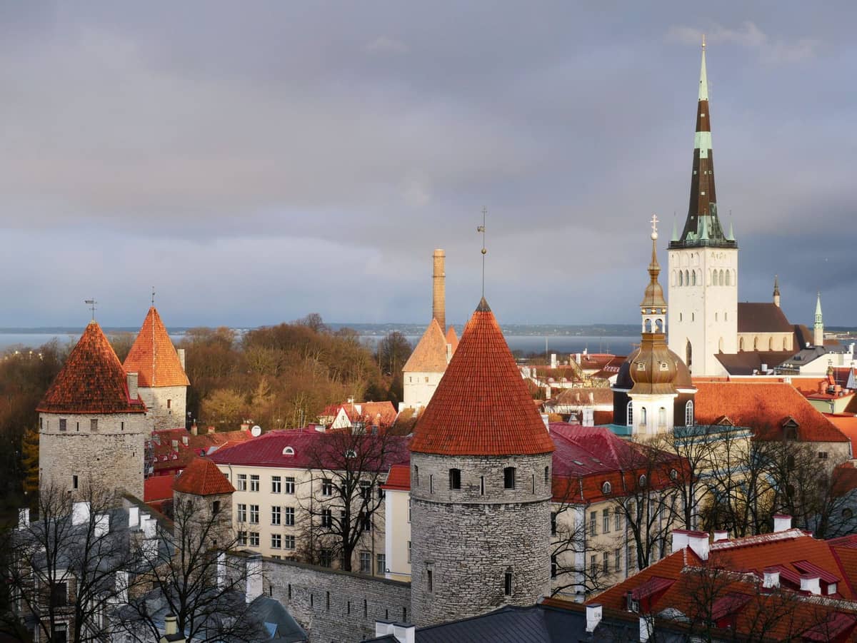 Skyline der Tallinner Altstadt mit mittelalterlichen Steintürmen, roten Dächern und dem hohen Turm der Olaikirche vor bewölktem Himmel.