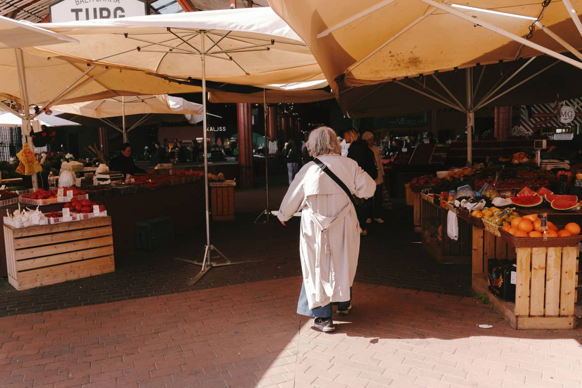 Person, die zwischen Freiluft-Marktständen unter Sonnenschirmen auf dem Balti Jaama Turg in Tallinn spaziert.