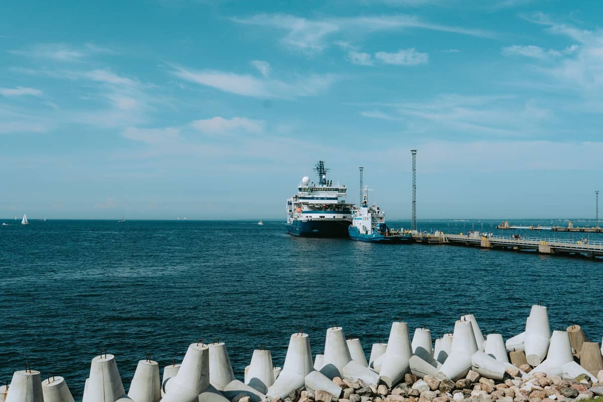 Große Fähre läuft bei blauem Sommerhimmel in den Hafen von Tallinn ein, mit Wellenbrecher und Meer im Vordergrund, was auf eine belebte Reisesaison hindeutet.