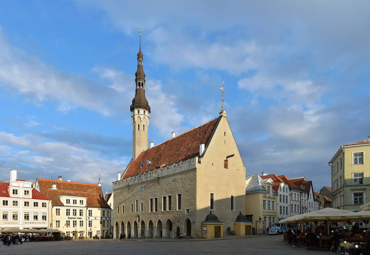 Das Tallinner Rathaus auf dem Rathausplatz an einem sonnigen Tag – mit vollständiger gotischer Fassade, rotem Dach und hohem Turm mit der berühmten Wetterfahne.