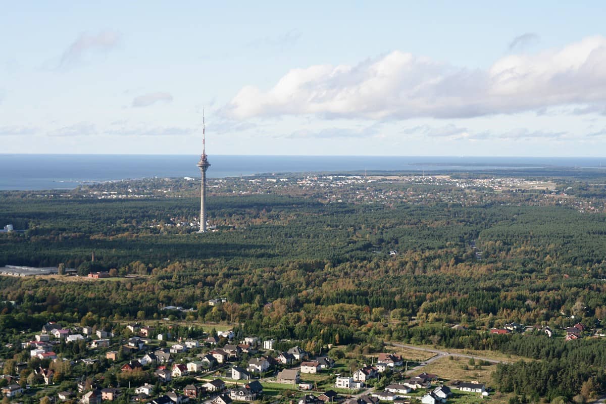 Der Tallinner Fernsehturm ragt über den umliegenden grünen Wald, im Hintergrund der Horizont der Ostsee unter einem teils bewölkten Himmel.