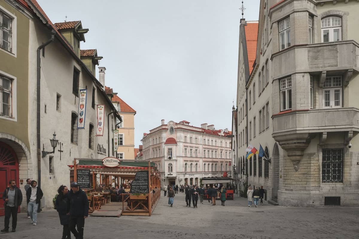 Kopfsteinpflasterstraße in der Tallinner Altstadt mit Fußgängern, historischen bunten Gebäuden, Cafés mit Außenbestuhlung und mittelalterlicher Architektur.