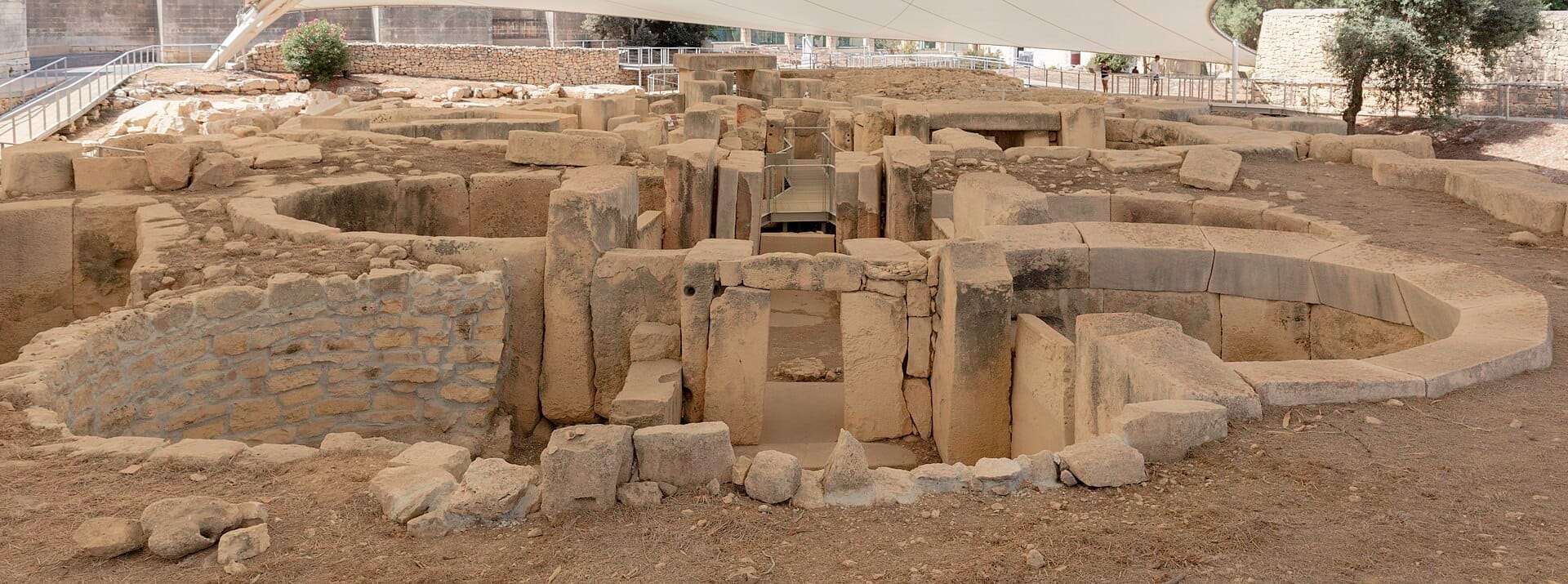 Le rovine preistoriche dei Templi di Tarxien, con grandi blocchi di pietra consumati e recinti circolari sotto una tettoia protettiva con percorsi sullo sfondo.