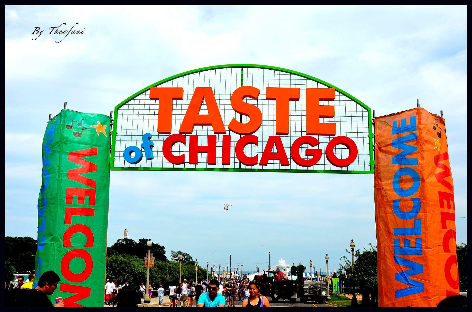 Un grande cartello del Taste of Chicago accoglie le folle al Grant Park sotto un cielo azzurro nuvoloso, con striscioni colorati e visitatori del festival in primo piano.