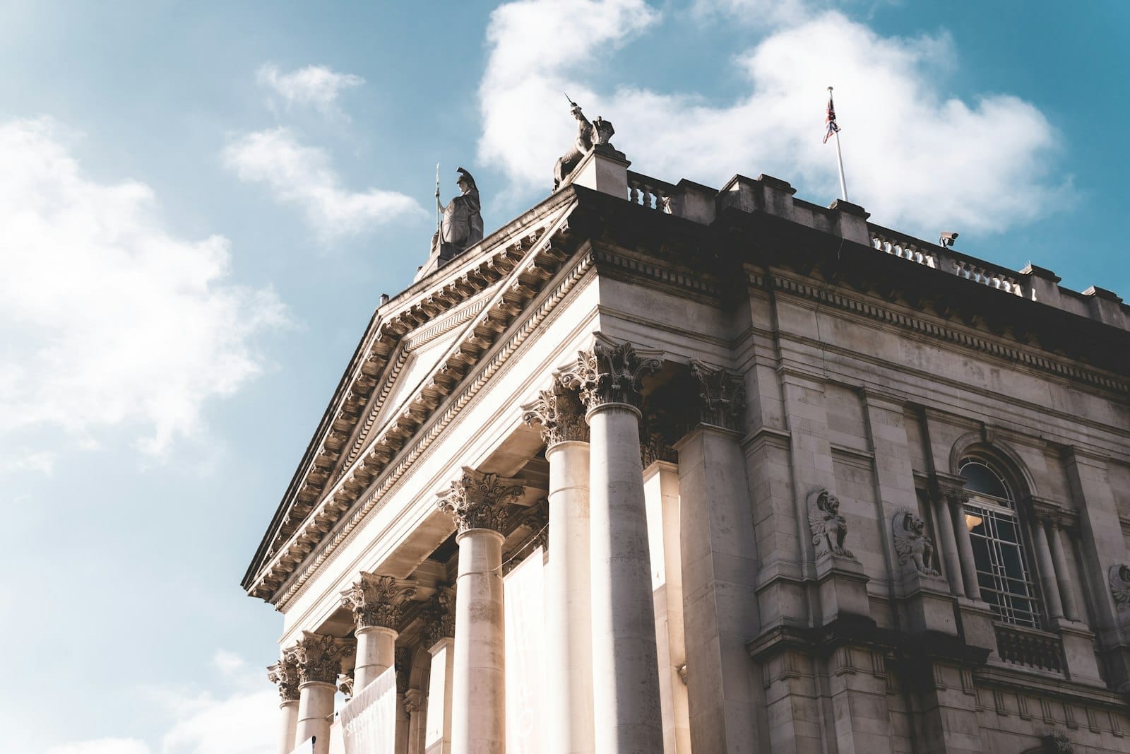 La facciata classica in pietra della Tate Britain con colonne e statue su uno sfondo di cielo azzurro con nuvole morbide.