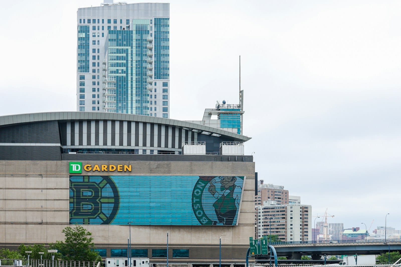 Vista frontale dell'arena TD Garden con i loghi dei Celtics e dei Bruins, sullo sfondo di moderni grattacieli e un cielo nuvoloso di Boston.