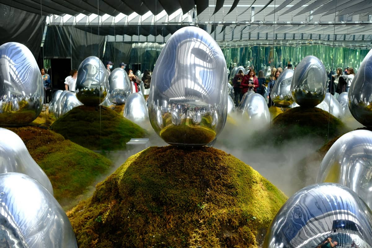 Visitors walk among reflective silver egg sculptures on mossy mounds surrounded by mist and mirrors inside teamLab Planets Tokyo.
