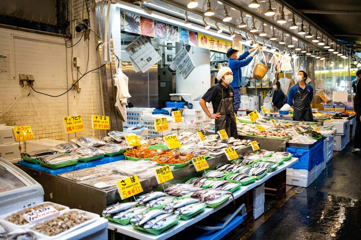 Brightly lit fish market with seafood stalls and workers, showcasing fresh produce in an indoor Tokyo market setting.