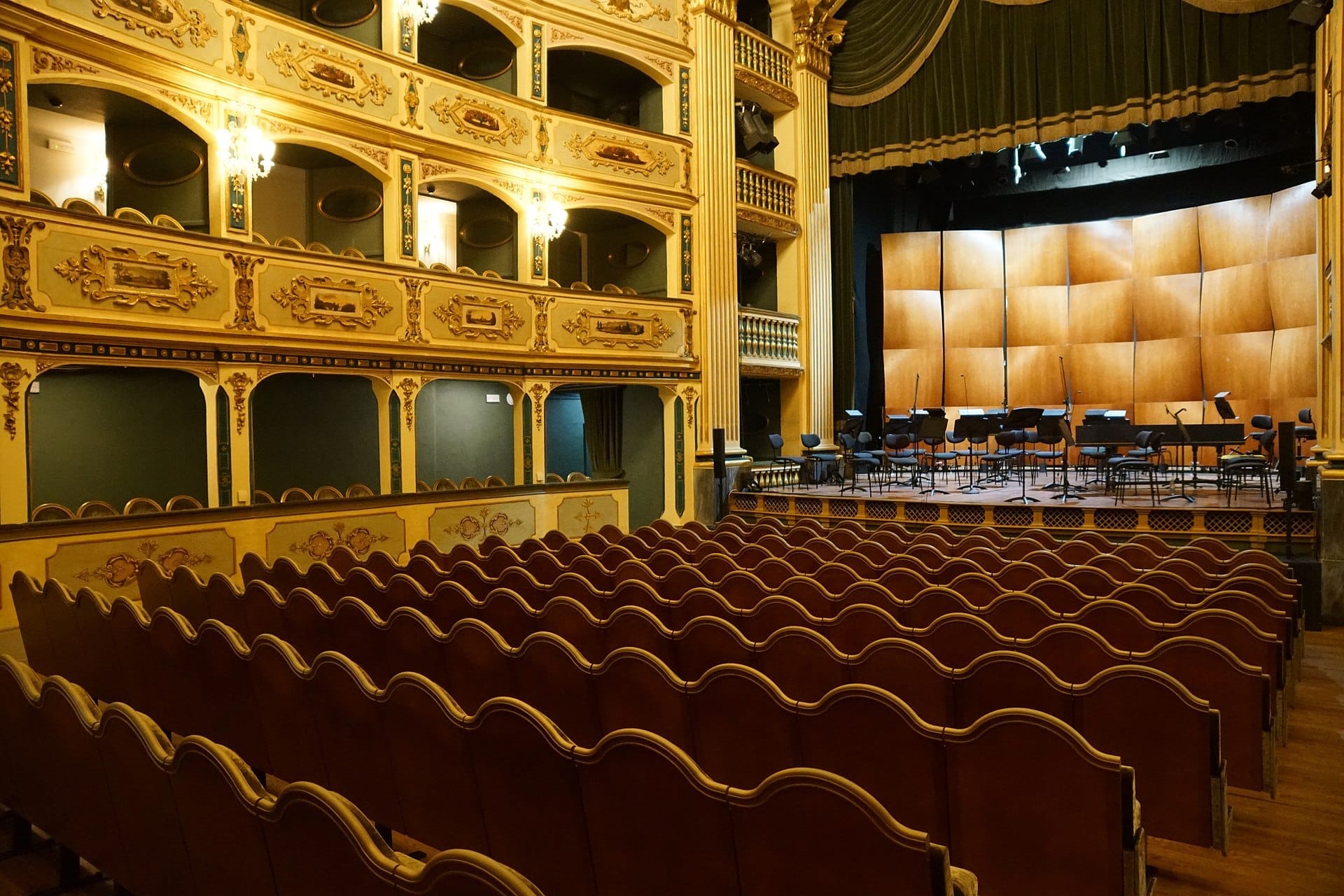 File di ornati sedili in velluto rosso di fronte al palcoscenico in legno del Teatru Manoel, circondati da balconi barocchi e dettagli dorati.