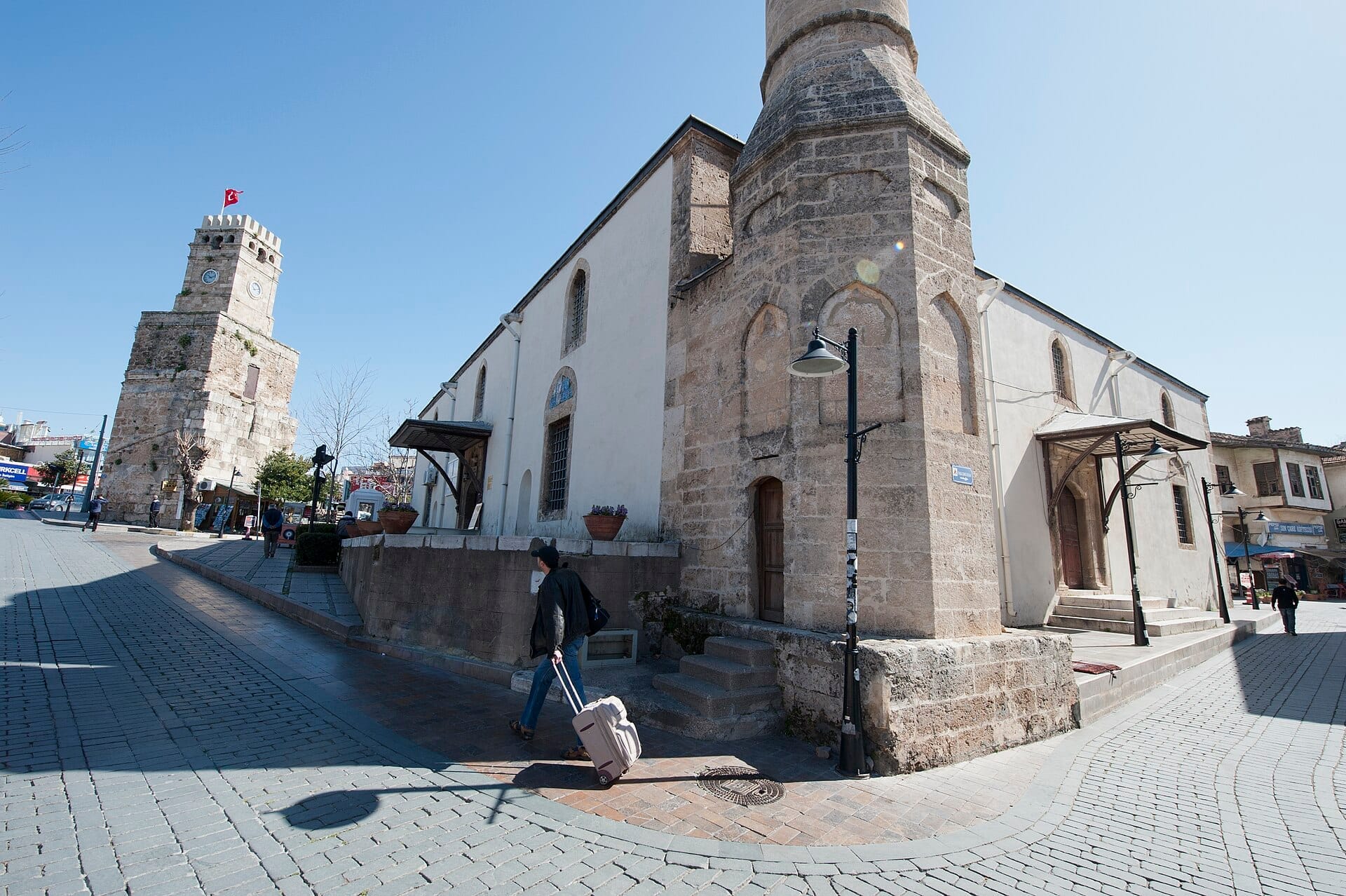La moschea Tekeli Mehmet Paşa con le sue mura in pietra e il minareto si erge accanto allo storico Torre dell'Orologio di Antalya su una soleggiata strada acciottolata.