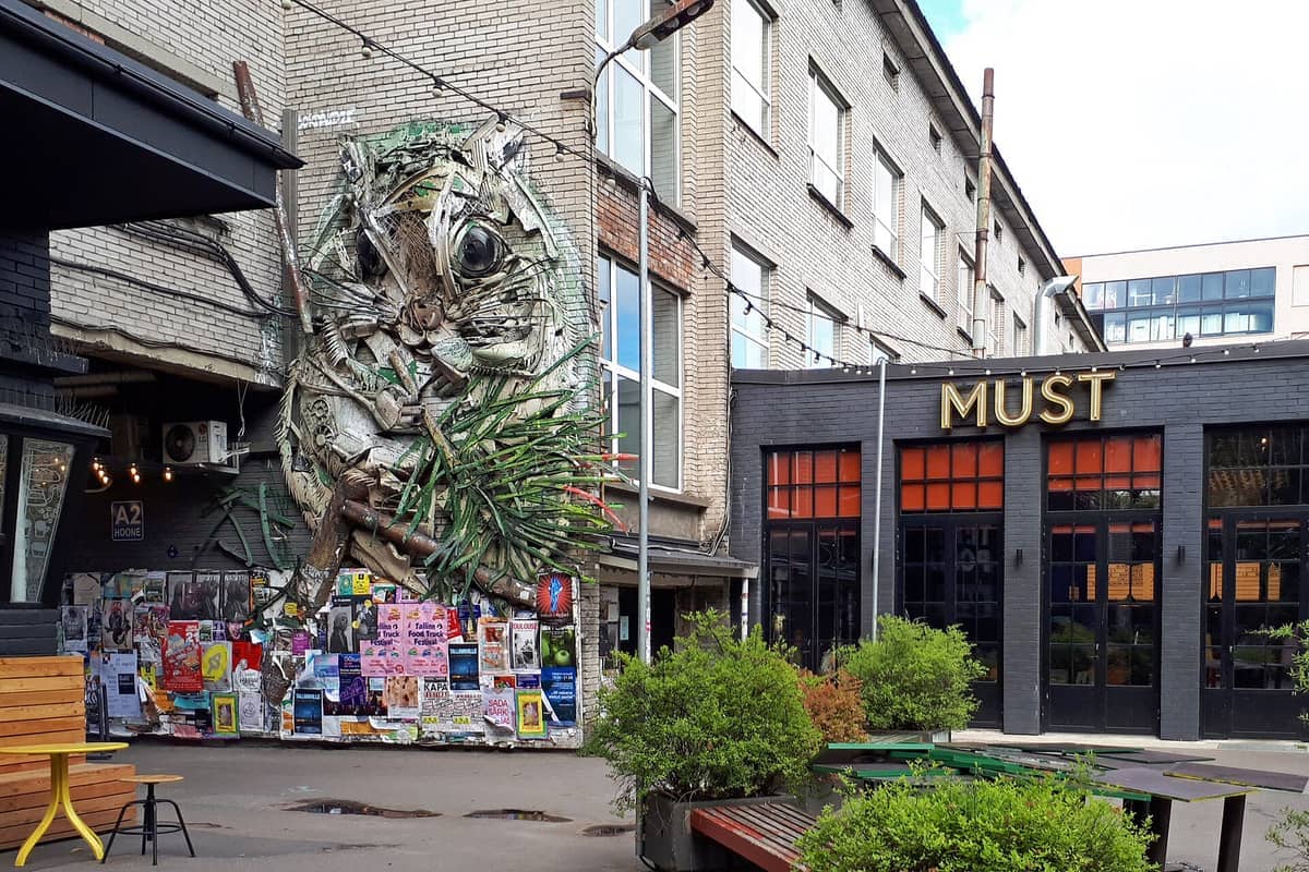 Der Hof der Telliskivi Creative City zeigt eine auffällige Tierskulptur aus recycelten Materialien, bunte Plakate, moderne Glasfenster und urbanes Grün in Tallinn.