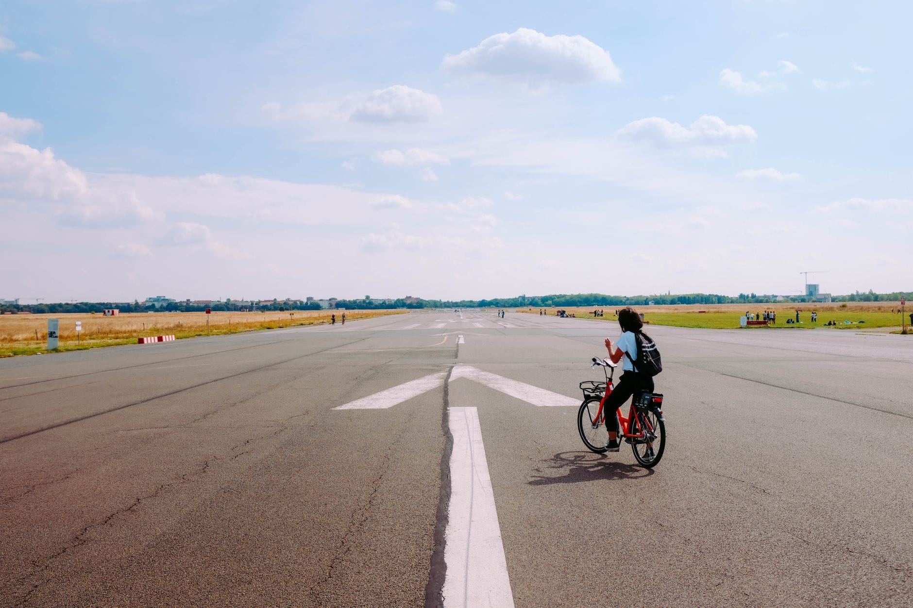 Una persona in bicicletta percorre la grande pista aperta del Tempelhofer Feld sotto un cielo blu con qualche nuvola sparsa.
