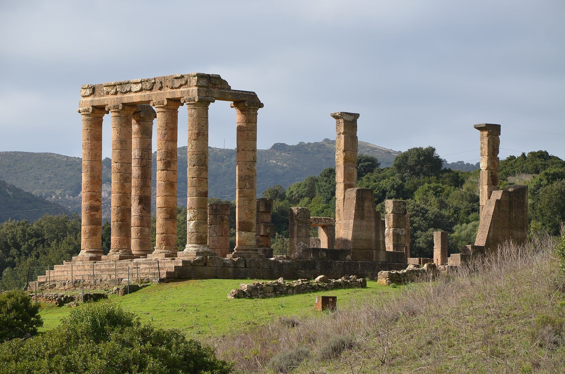 Die antiken Säulen und Steinruinen des Tempio di Antas ragen über grünes Gras und Bäume in den bewaldeten Hügeln des Sulcis-Iglesiente auf Sardinien empor.