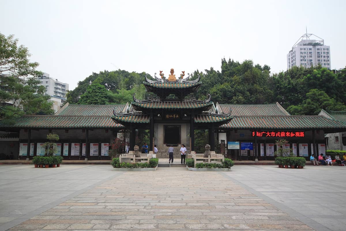 Main entrance to the Temple of the Five Immortals in Guangzhou, featuring a traditional green-tiled roof and modest courtyard surrounded by trees and city buildings.
