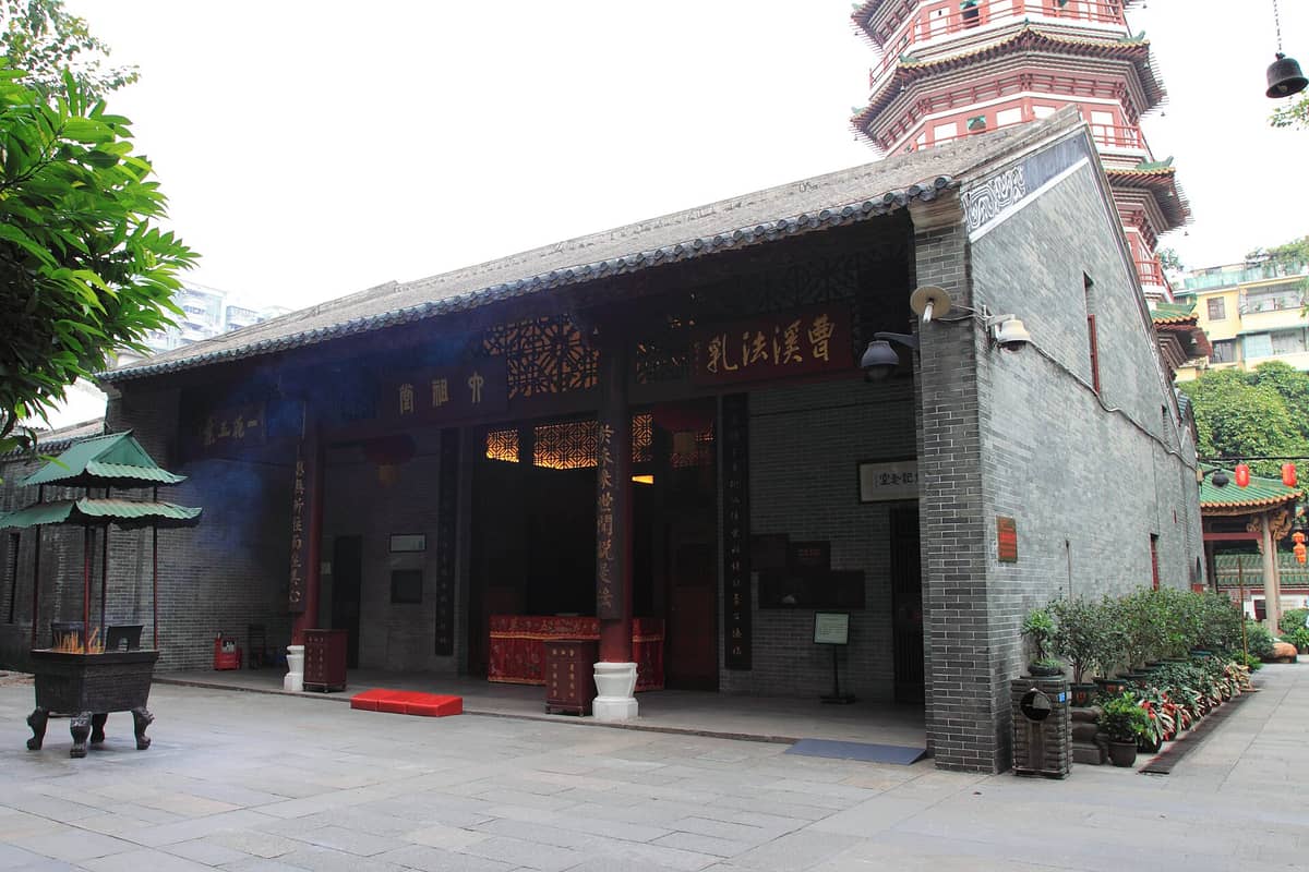 Entrance to the Temple of the Six Banyan Trees with the distinct multi-story Flower Pagoda visible in the background and incense smoke rising.