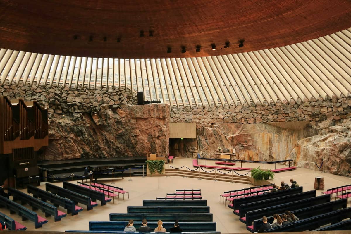 Interior da Igreja Temppeliaukio com paredes circulares de granito bruto, teto com cúpula de cobre, bancos de madeira e o altar ao centro.